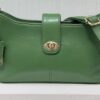 Green leather handbag with gold-tone hardware and an adjustable strap resting on a white surface.