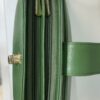 Green leather bag opened to reveal two side-by-side zippered compartments with gold-tone zipper pulls and a green strap visible.