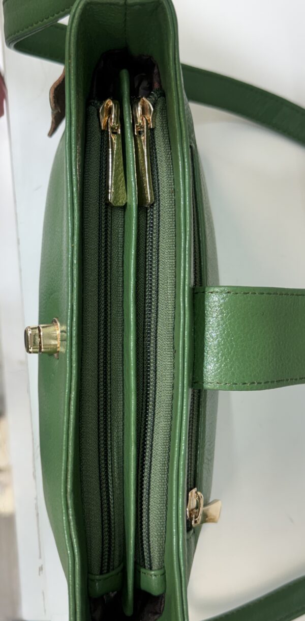 Green leather bag opened to reveal two side-by-side zippered compartments with gold-tone zipper pulls and a green strap visible.