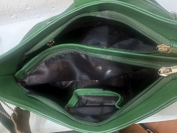 Open green handbag showing inner zipper compartments and dark lining