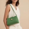 Model posing with a green shoulder bag against a beige background, wearing a white sleeveless top.
