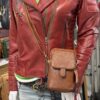Red leather biker jacket on a mannequin with a brown textured crossbody bag and a green-and-white striped top visible underneath.