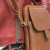 Close-up of a red leather jacket zipper beside a brown textured leather bag with gold hardware. This image shows a red jacket with a zipper and a brown leather bag with metal clasps.