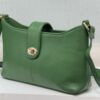 Green leather handbag with gold hardware resting on a white surface, shown from a side angle.