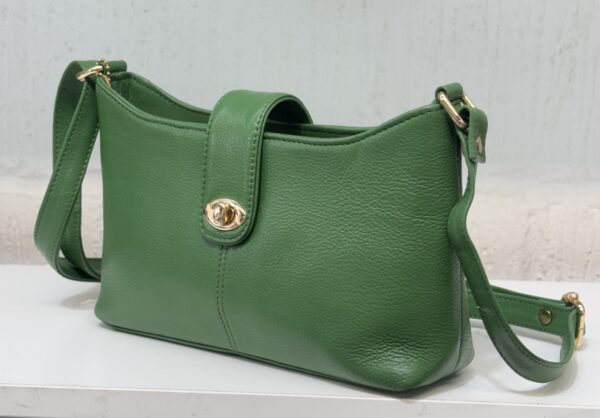 Green leather handbag with gold hardware resting on a white surface, shown from a side angle.