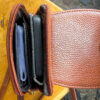Brown leather wallet opened to reveal card slots and a zipped compartment with a blue card visible? inside.