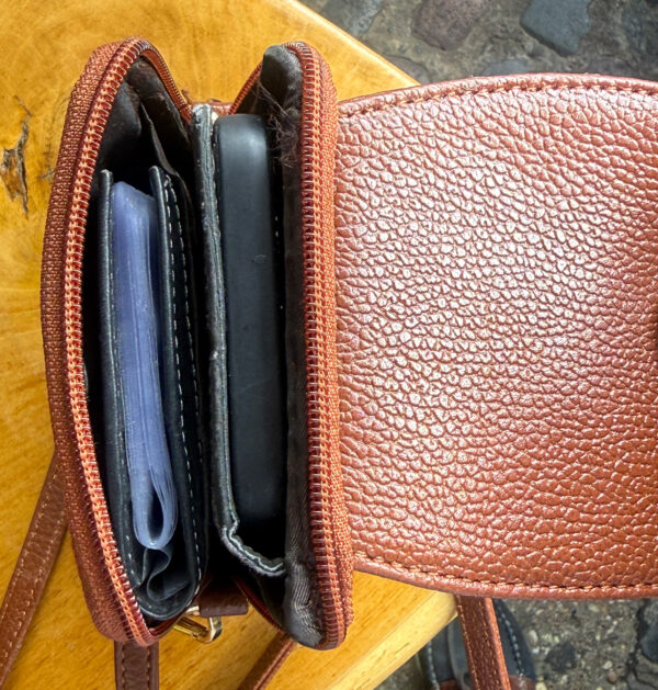 Brown leather wallet opened to reveal card slots and a zipped compartment with a blue card visible? inside.